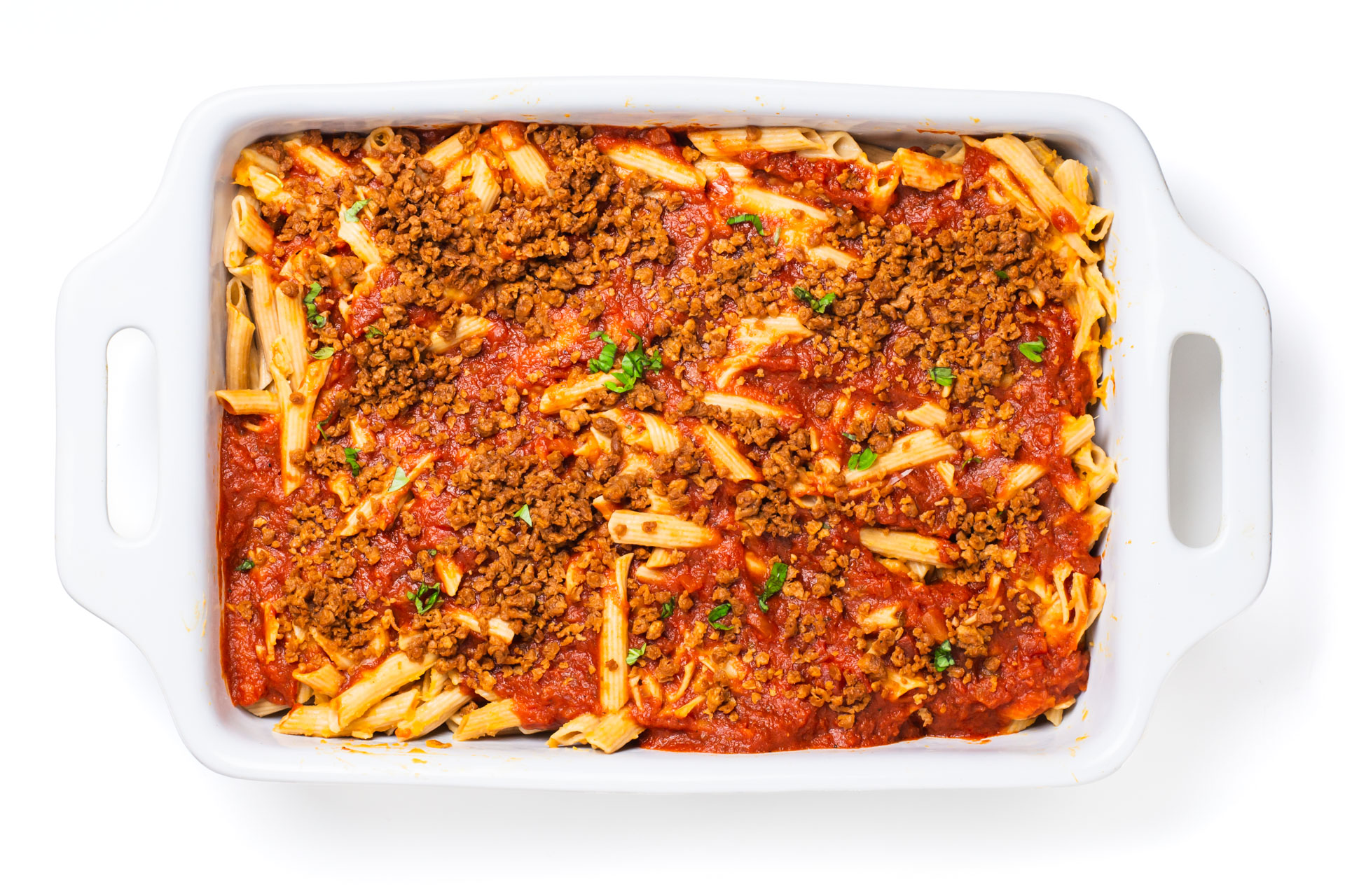Looking down on a casserole dish full of this cooked penne topped with red sauce and veggie crumbles.