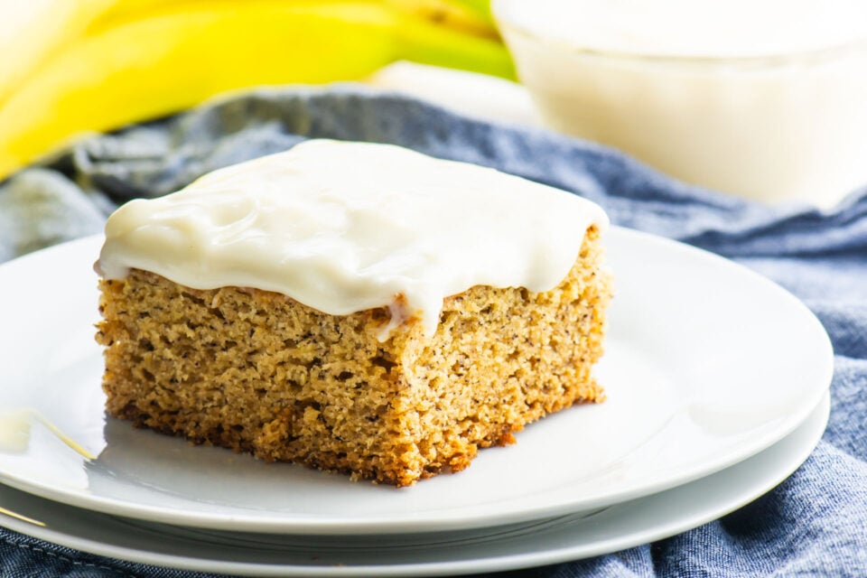 A slice of Vegan Banana Cake sits on a plate in front of bananas.