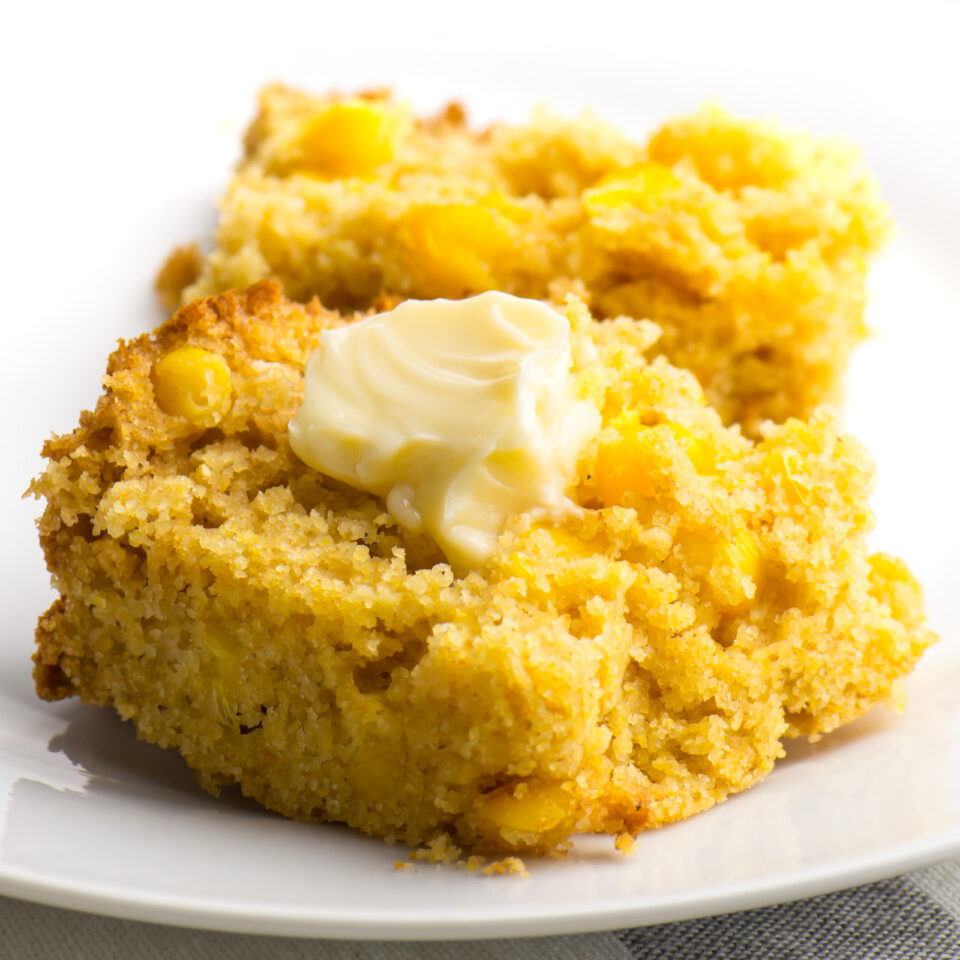 A slice of vegan cornbread cut in half with butter melting on one side.