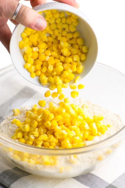 Pouring whole kernel corn into a mixing bowl with flour and cornmeal.