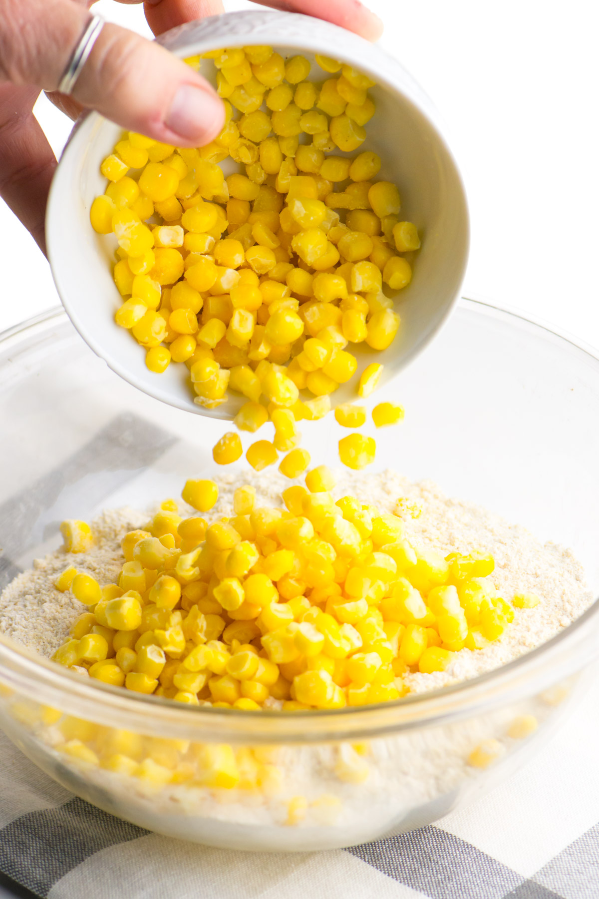 Pouring whole kernel corn into a mixing bowl with flour and cornmeal.