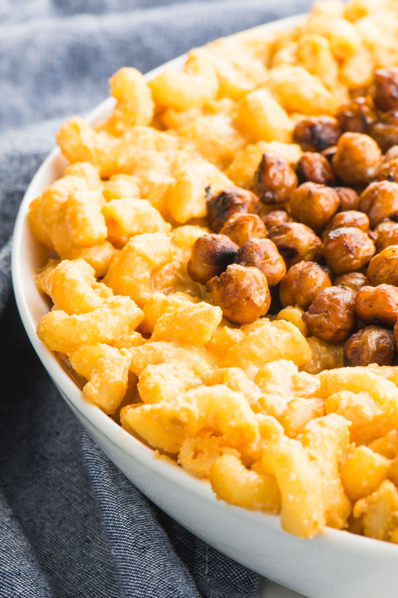 Closeup of Vegan Stovetop Mac and Cheese with Smoky Chickpeas in a white bowl next to a blue kitchen towel