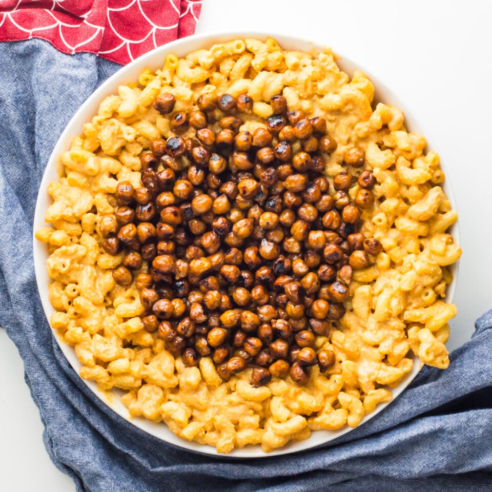 Looking down on a bowl full of vegan stovetop mac and cheese with chickpeas in the center. A blue kitchen towel surrounds the bowl.