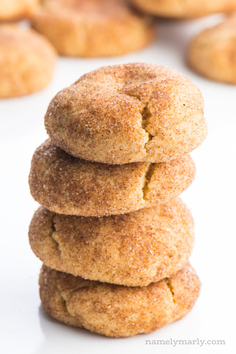 A stack of four snickerdoodles cookies sit one on top of the other, with lots of cinnamon sugar coating. There are several cookies in the background.