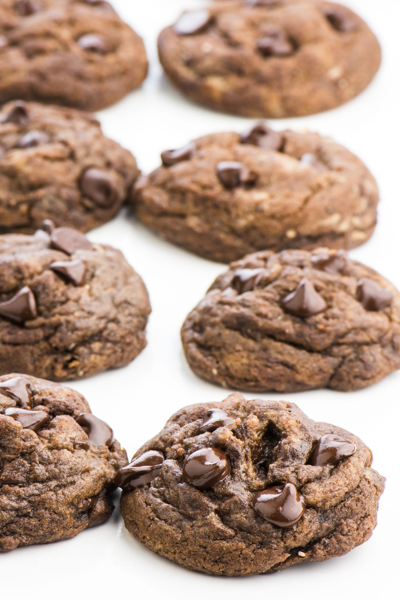 Eight chocolate chocolate chip cookies are lined in rows of four on a white countertop.