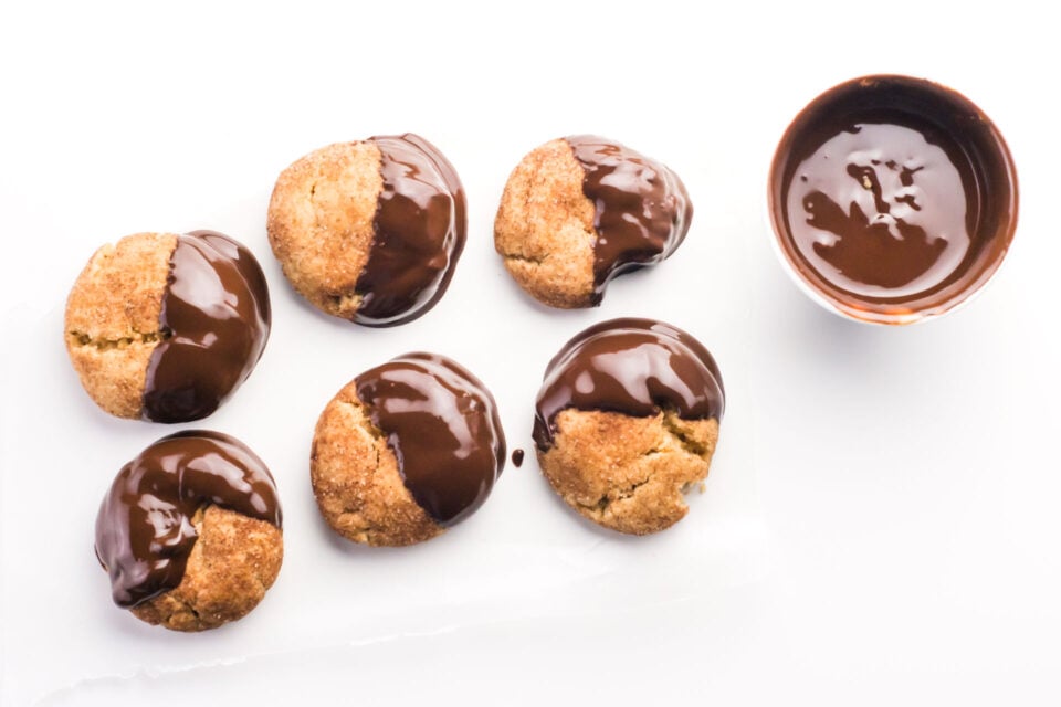 This angle is looking down on a row of chocolate-dipped snickerdoodles with a bowl of melted chocolate sitting beside them.