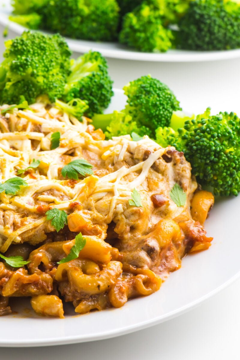 Vegan Macaroni Casserole is on a white plate with stated broccoli in the background.
