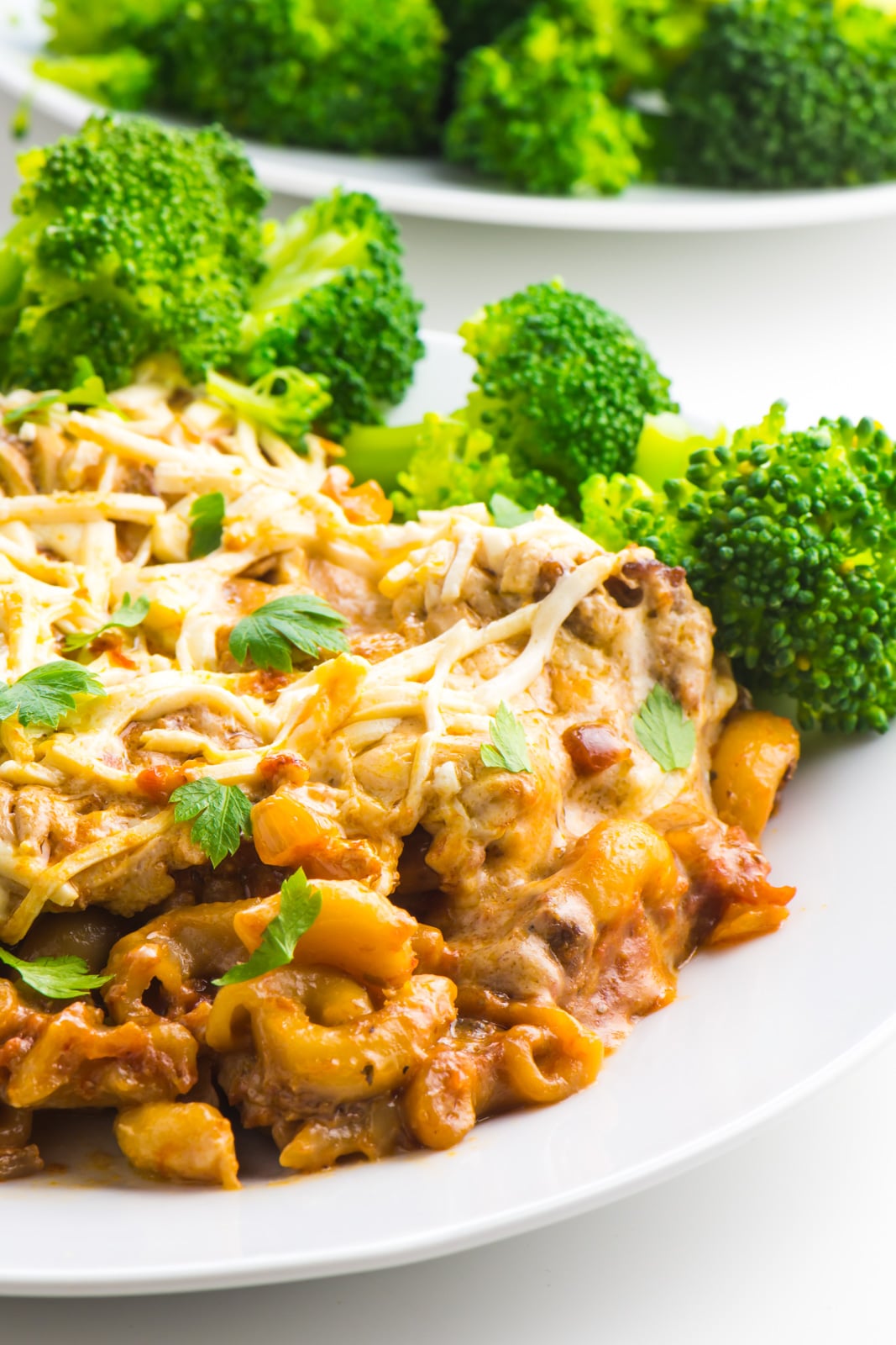 Vegan Macaroni Casserole is on a white plate with stated broccoli in the background.