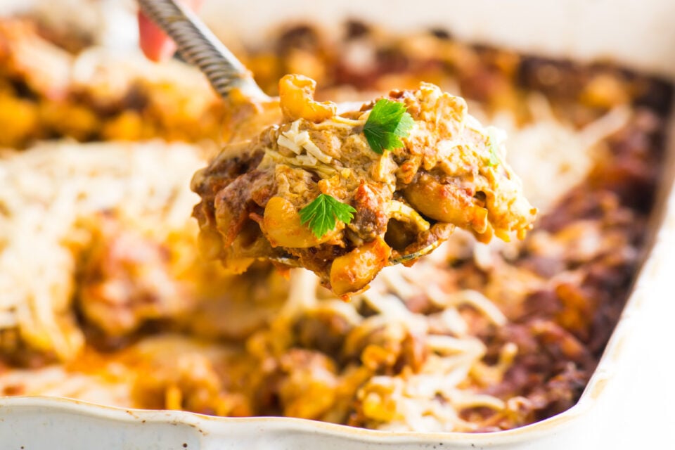 A serving spoon is coming out of a baking dish, showing a spoonful of cheesy vegan dinner!