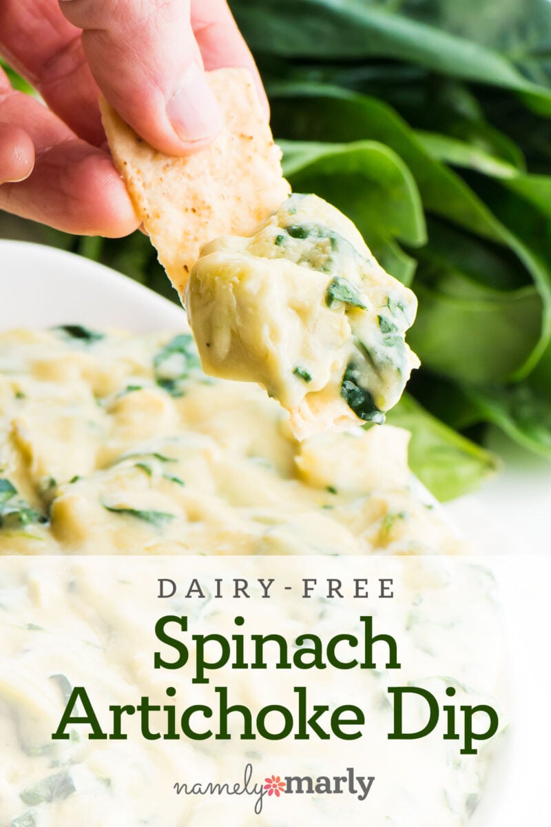 A hand holding a chip with spinach artichoke dip on it