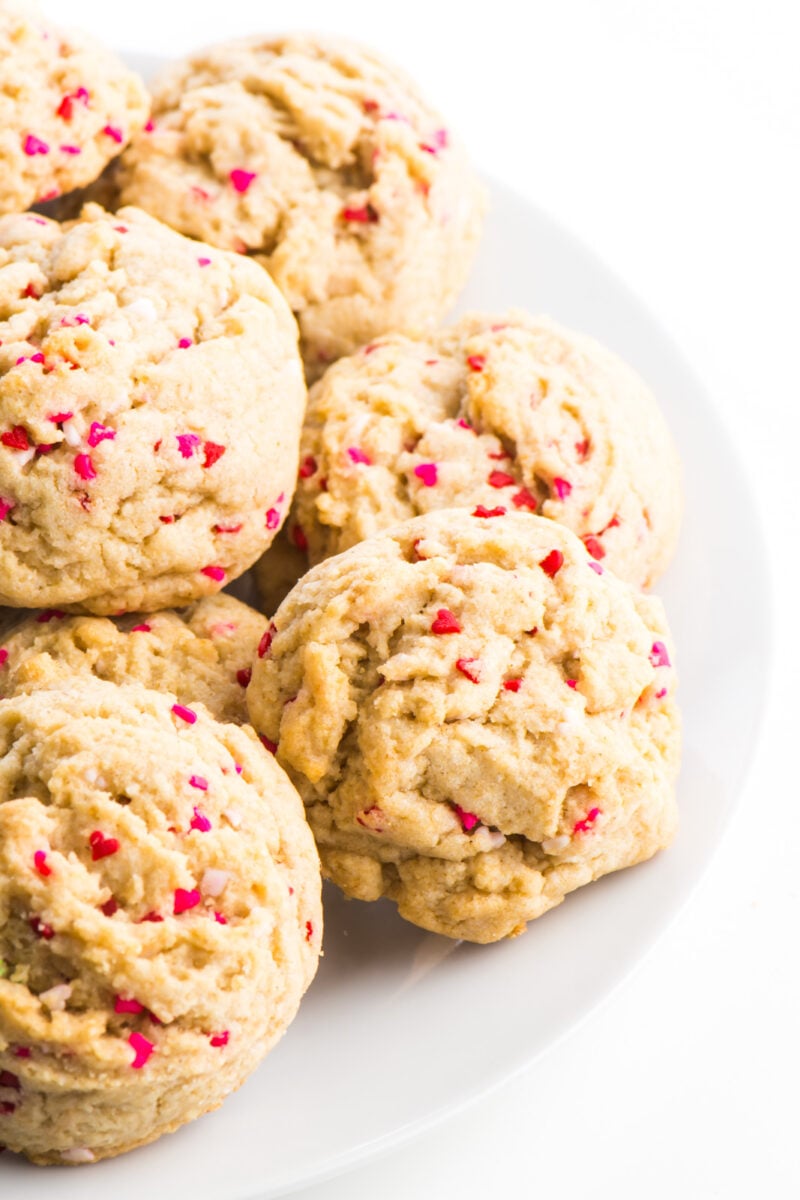 A white plate is stacked high with valentines cookies, which are basically sugar cookies with heart-shaped sprinkles.