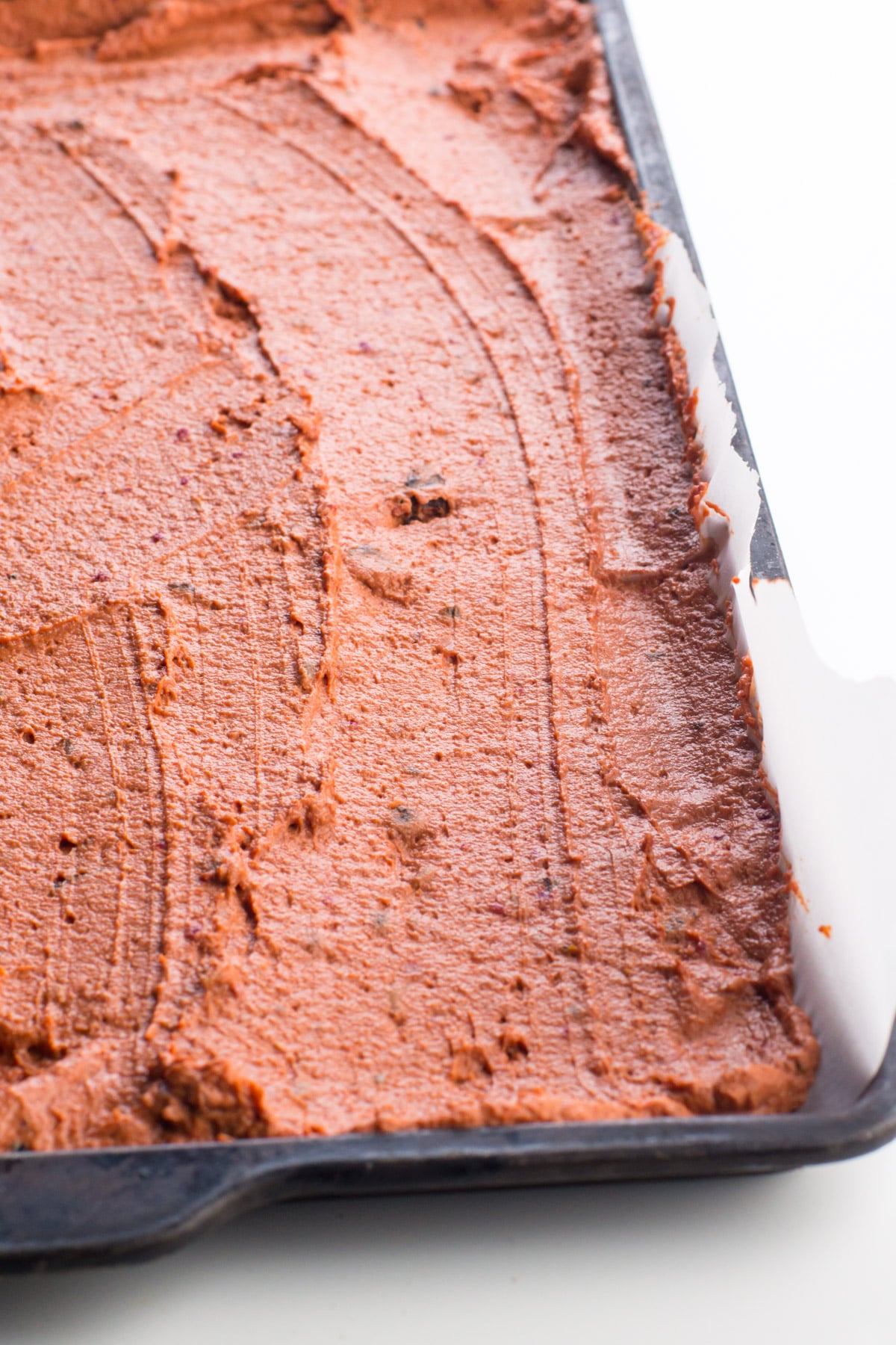 Vegan pepperoni dough in a sheet pan lined with parchment paper and spread out across the pan.