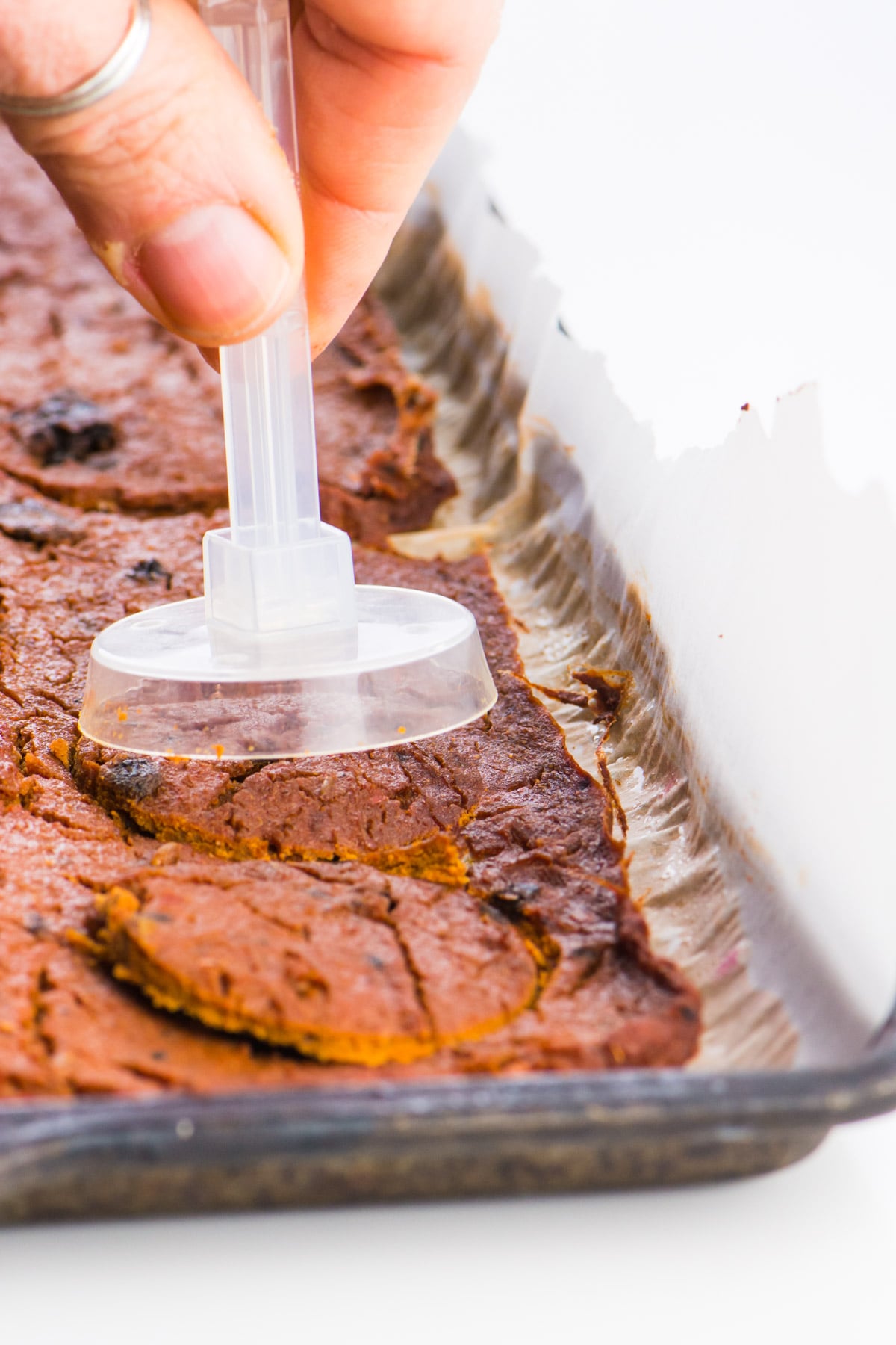 A round cutting utensil is hovering over baked vegan pepperoni.