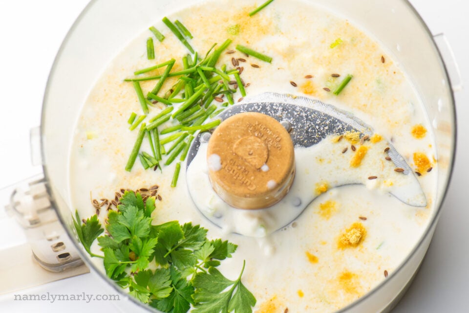 A food processor bowl is full of ingredients to make homemade salad dressing.