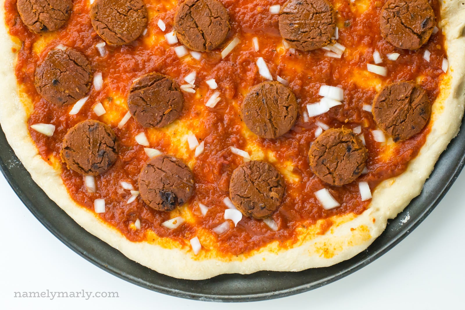 Looking down on a cheeseless pizza, with onion bits between slices of veggie meat.