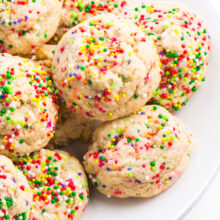 A white plate has several colorful confetti cookies, sugar cookies with sprinkles baked right into the dough.