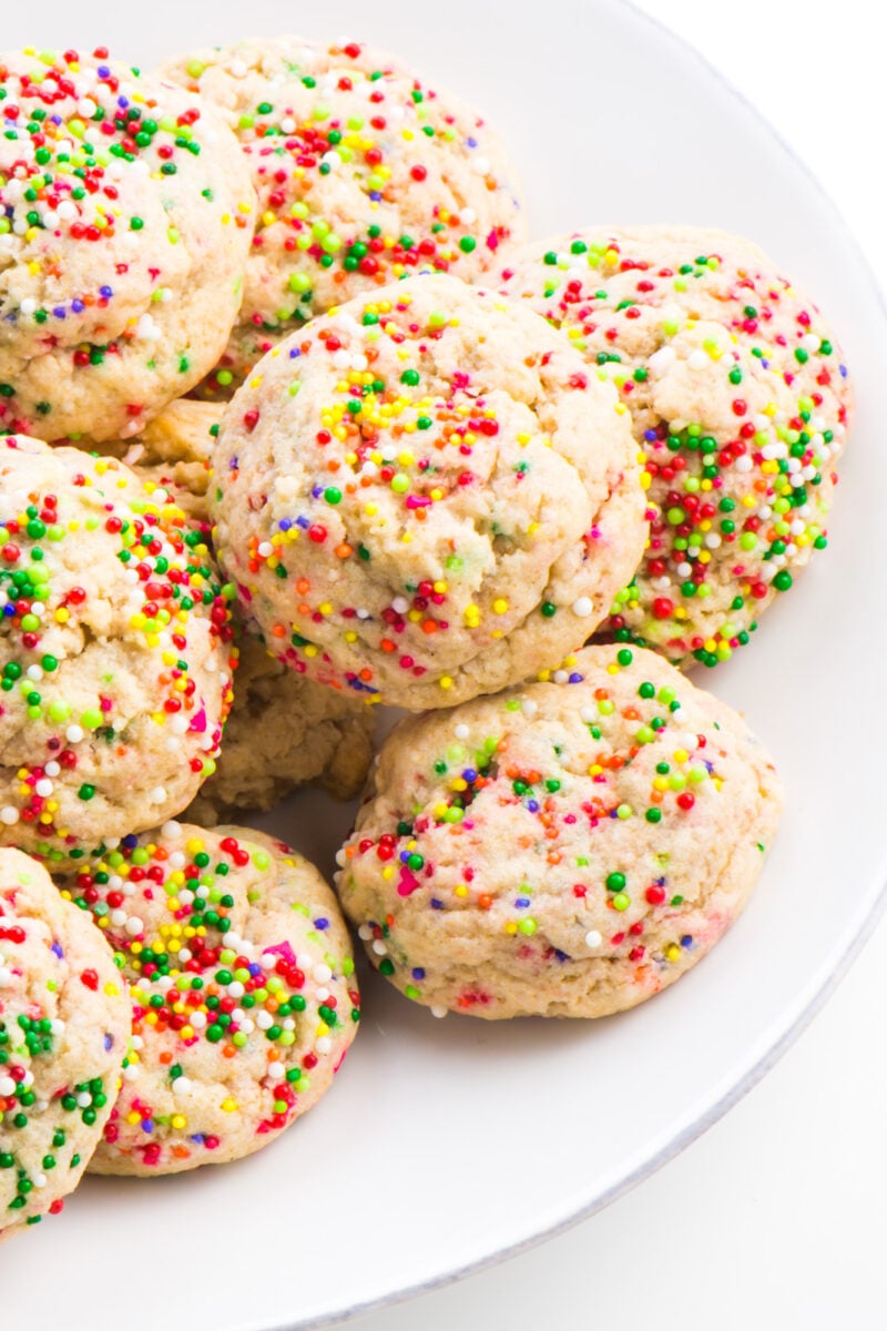 A white plate has several colorful confetti cookies, sugar cookies with sprinkles baked right into the dough.