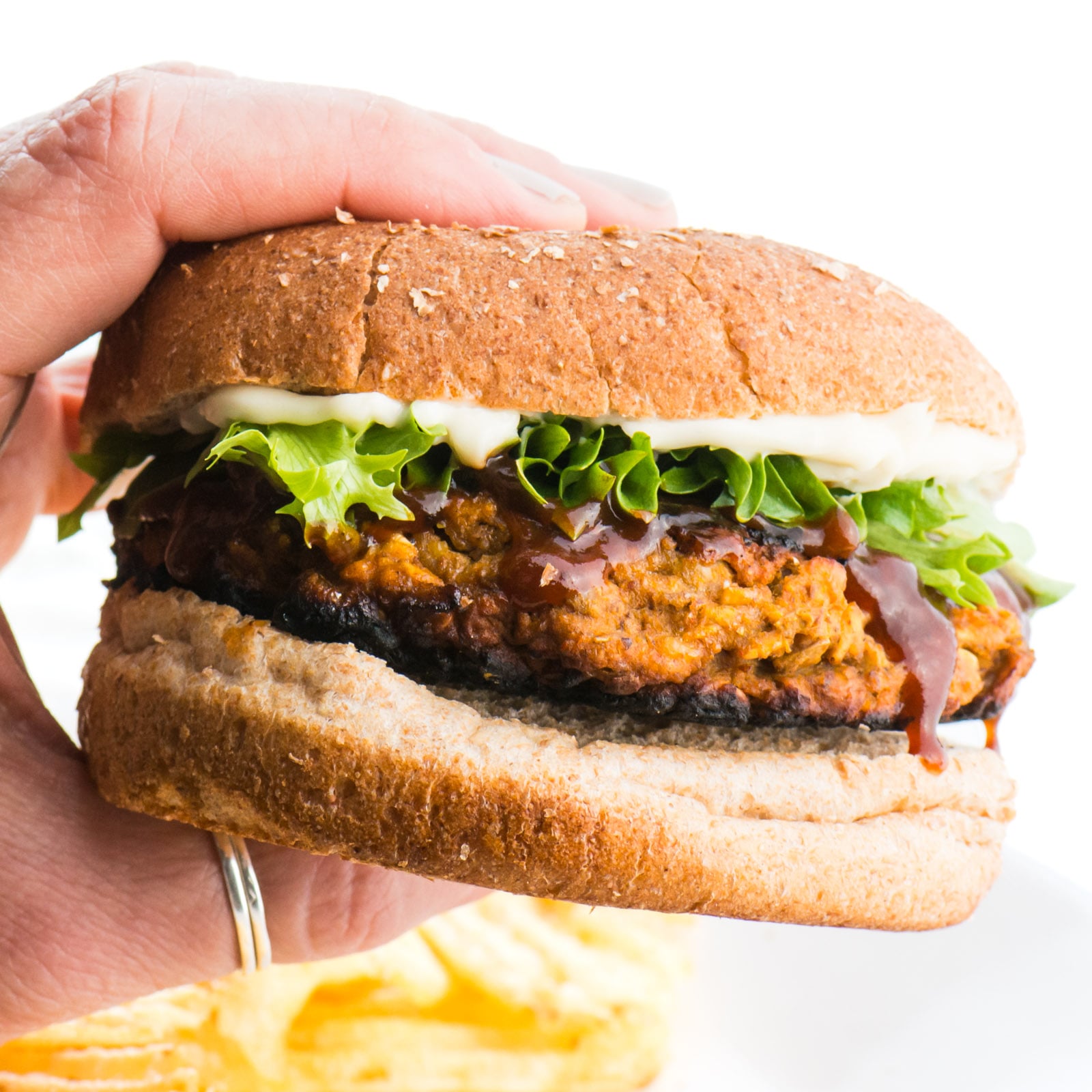 A hand holds a veggie burger, showing off greens and mayo on a whole wheat bun.