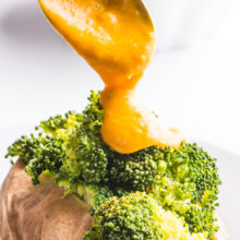A spoon drizzles vegan cheese sauce over steamed broccoli.