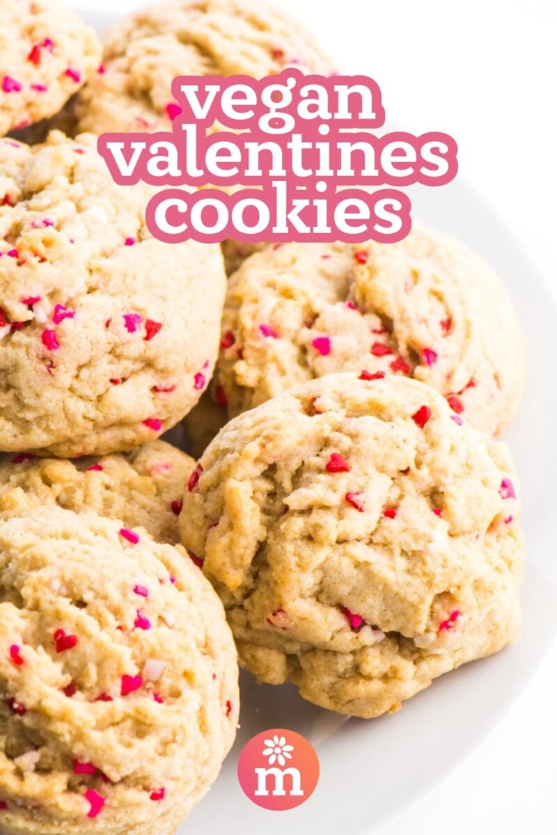 A plateful of colorful sugar cookies sits on a white counter. The text reads, vegan valentines cookies.