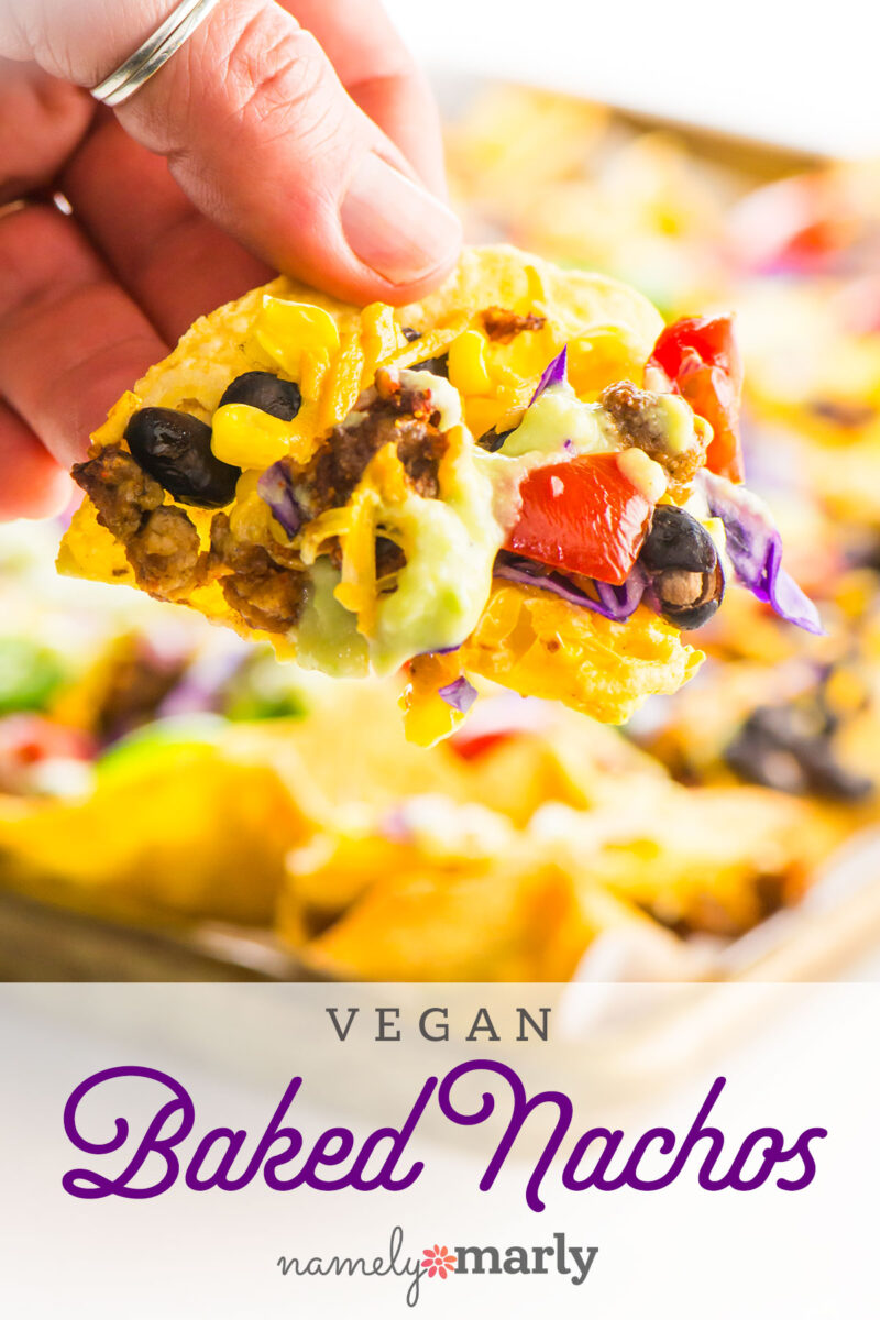 A hand holds a tortilla chip loaded with nacho ingredients with text that reads Vegan Baked Nachos