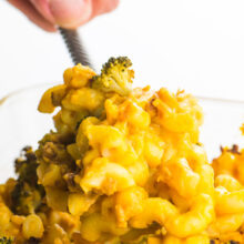 A hand reaches in and scoops out some vegan mac and cheese casserole from the dish.