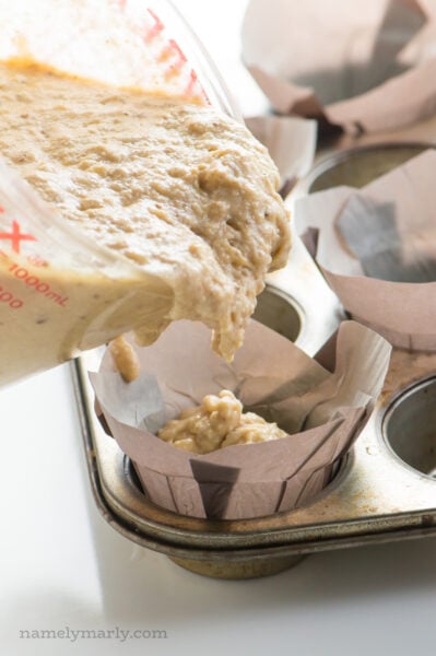 The measuring glass is being used to pour muffin batter into papers in a muffin tin.
