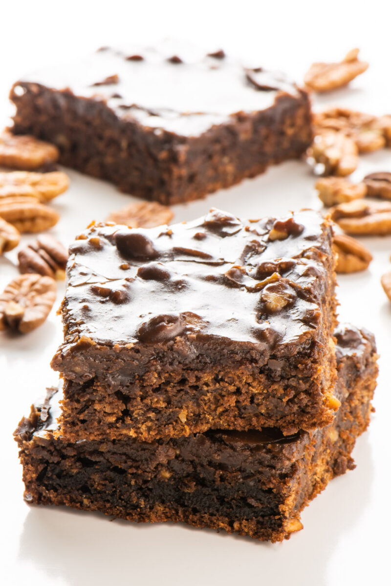 Slices of vegan Texas sheet cake are stacked on top of each other with more slices and pecans around it.