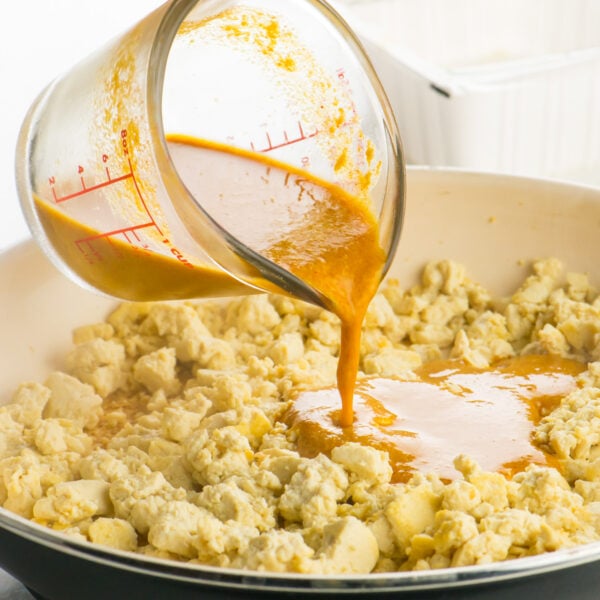 Pouring the sauce into tofu crumbles in the skillet.