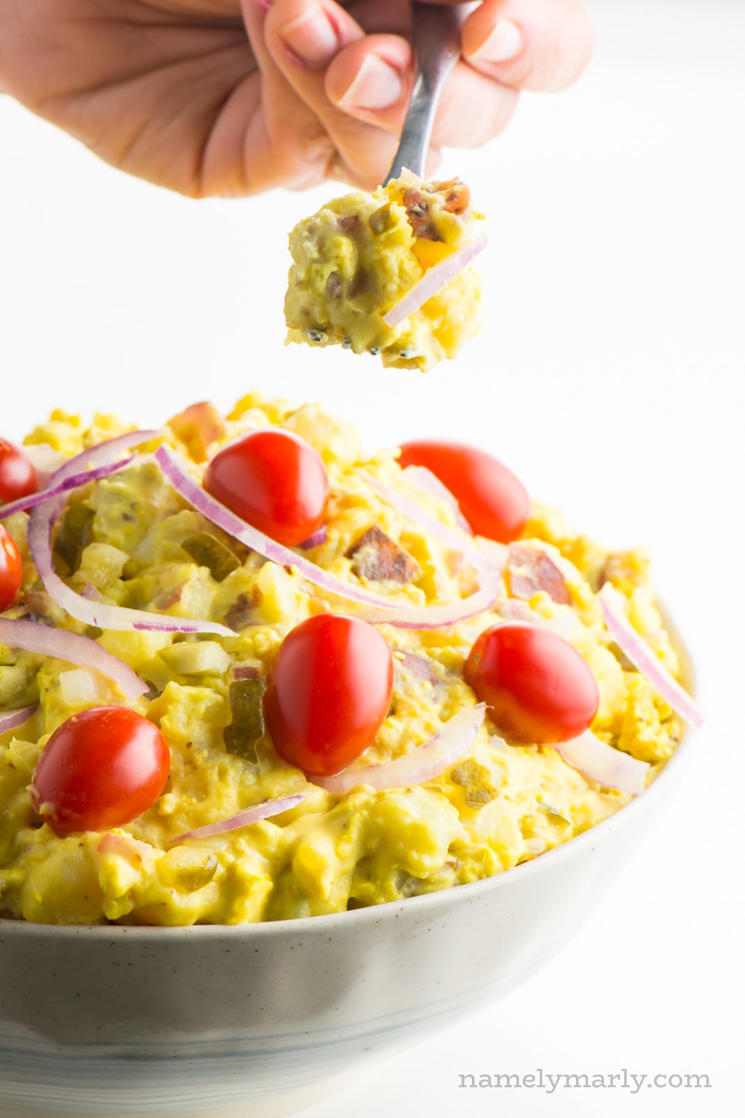 A hand holds a spoonful of vegan potato salad over the rest of the bowl.