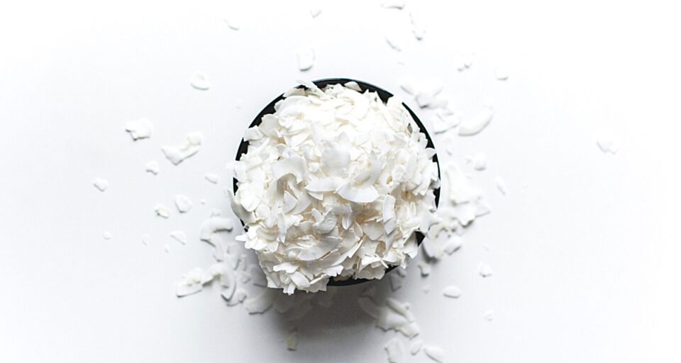 Looking down on a wooden bowl full of coconut flakes that spill over onto the white counter around the bowl.