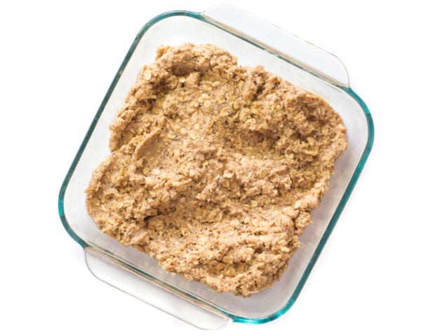 The batter for oatmeal bars has been pressed into the bottom of a square baking pan.