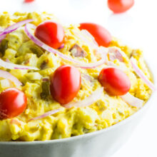 A bowl of vegan potato salad with cherry tomatoes on the salad and behind it.