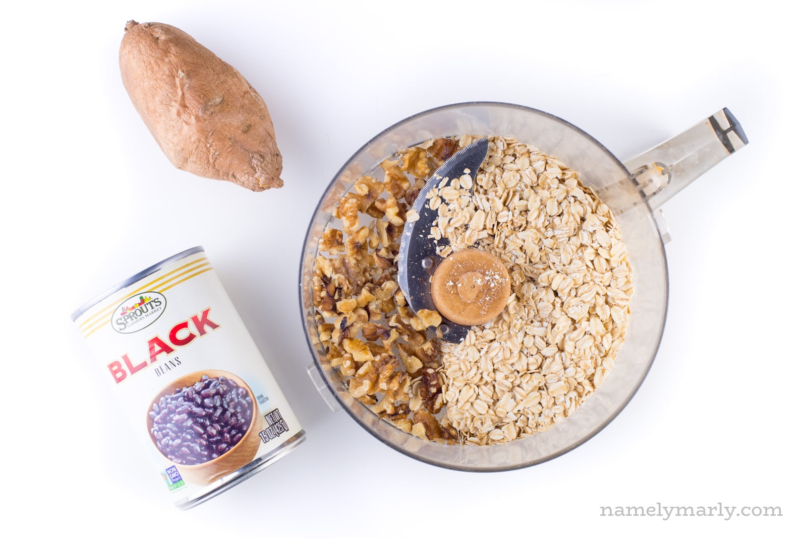 Oatmeal and walnuts are in a food processor with a sweet potato and can of black beans next to it.