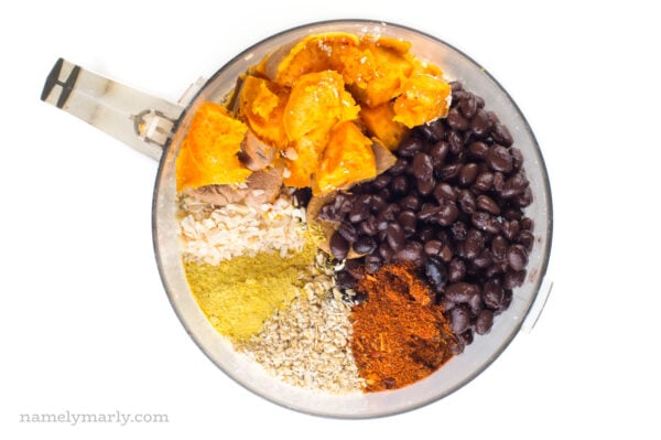 Ingredients plus spices for these black bean burgers are in a food processor.