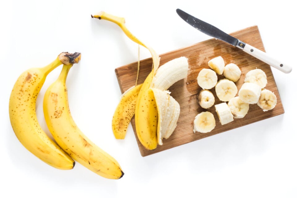A banana on a cutting board with several chopped bananas next to it.