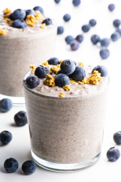 A glass full of blueberry overnight oats is in the foreground with blueberries and granola on top and another glass behind it.