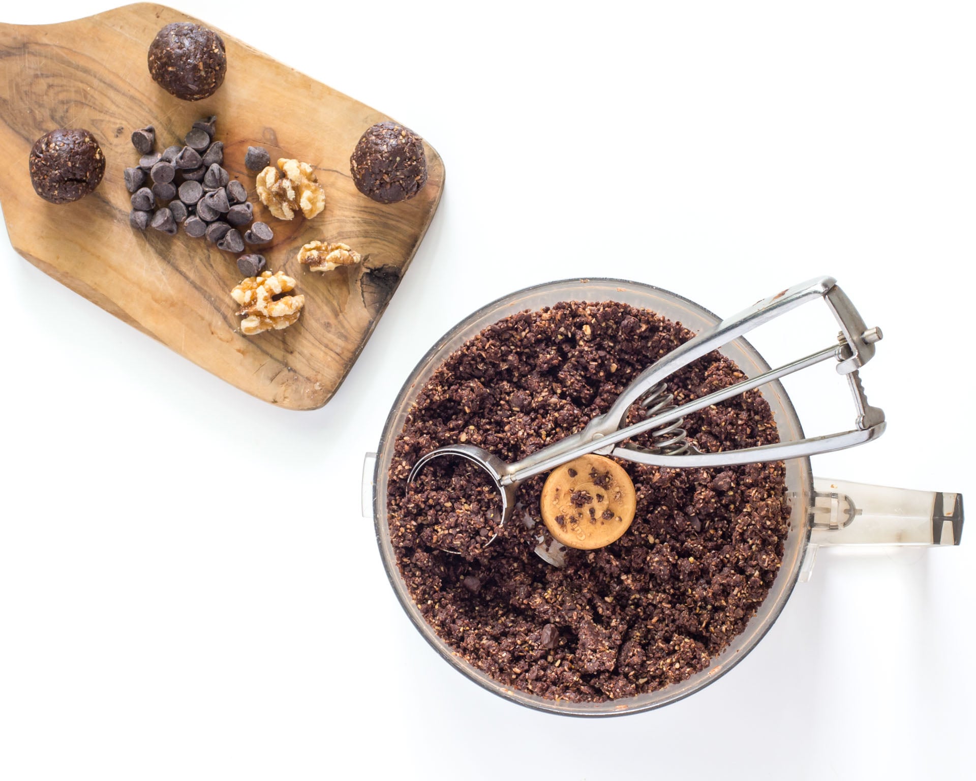 A cookie dough scoop is used to create energy bites. Finished bites are on a small cutting board.