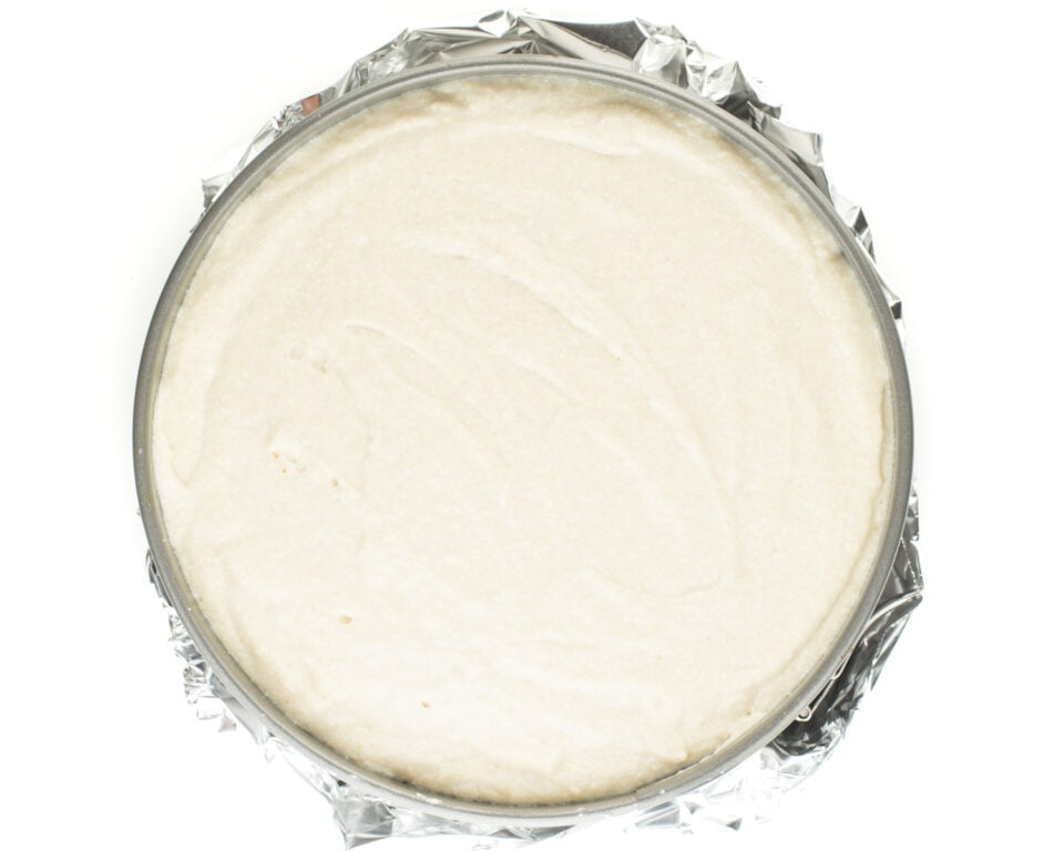Raw cheesecake is in a pan wrapped with aluminum foil.