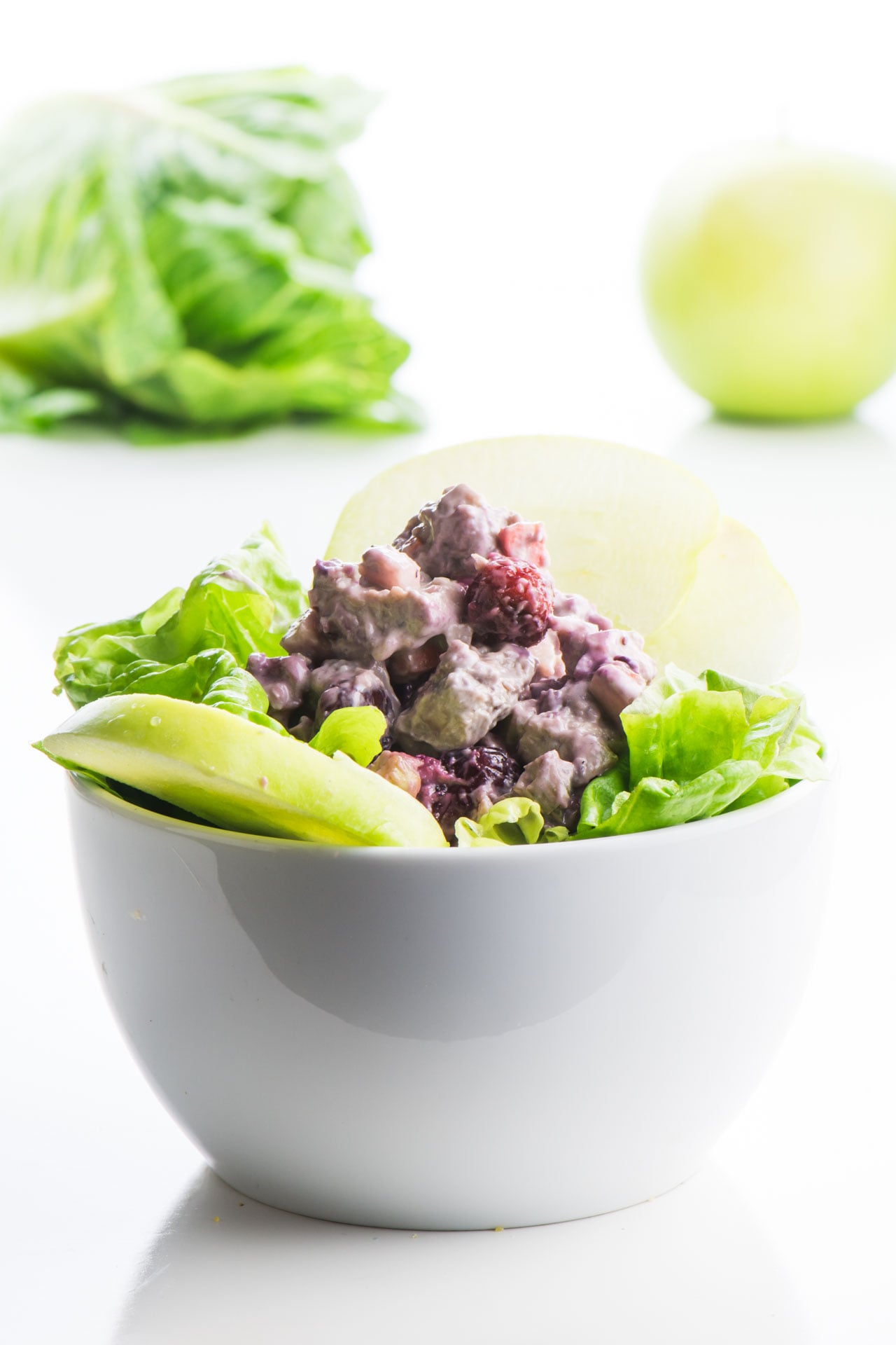 Vegan chicken salad is piled high over greens and sliced green apples.