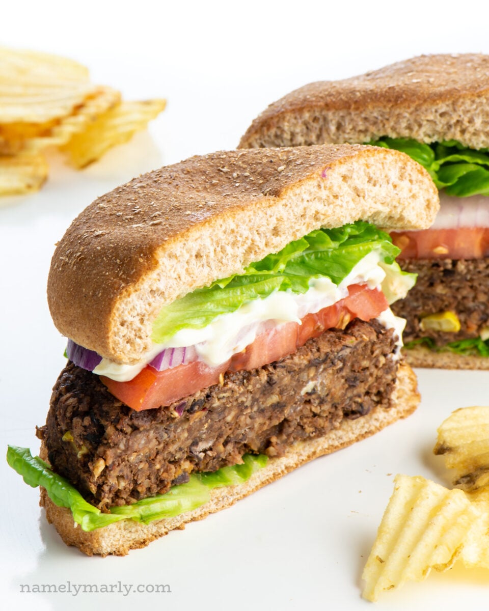 A sweet potato black bean burger on a bun is cut in half showing sliced tomatoes and red onions.