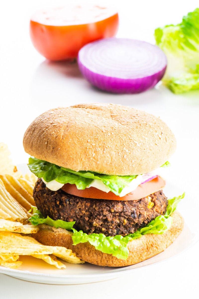 A sweet potato black bean burger sitting on a plate with potato chips beside it.