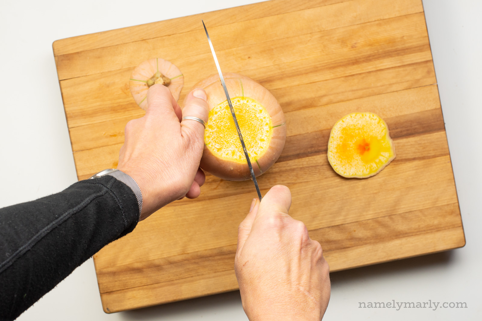 One hand holds a butternut squash while the other pushes down on it with a knife to cut it in half.