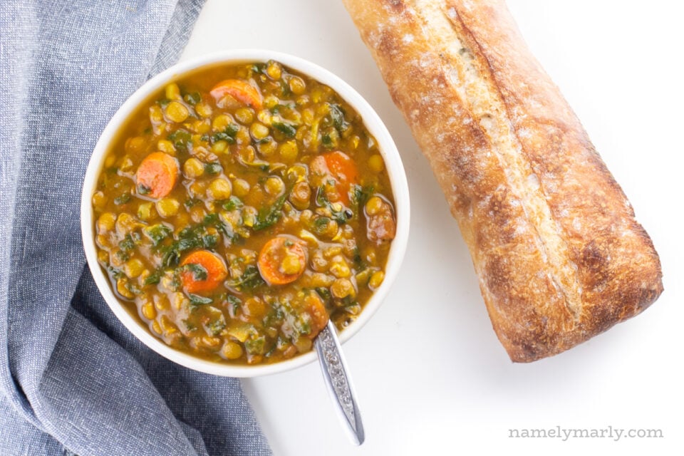 Looking down on a bowl of curried lentil soup with a loaf of bread beside it.