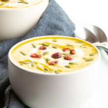 Two bowls of vegan butternut squash soup sit next to each other with two spoons behind it.