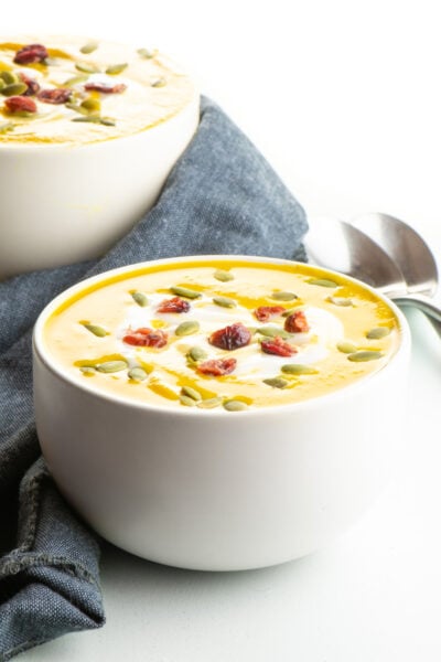 Two bowls of vegan butternut squash soup sit next to each other with two spoons behind it.