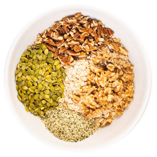 A large white bowl holds oats, nuts, and seeds for granola.