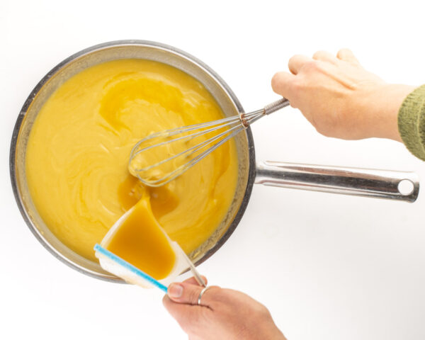 One hand stirs the gravy while another had pours in vegetable broth.