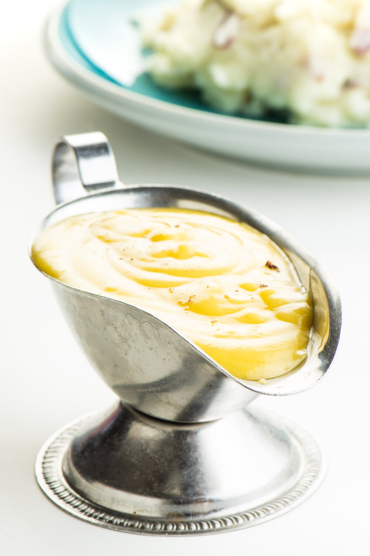 Gravy in a serving boat, with a plate of mashed potatoes behind it.