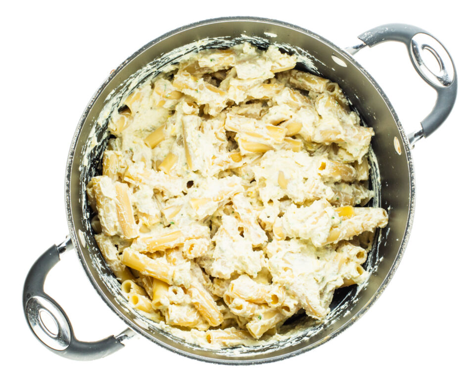 Vegan ricotta has been poured over cooked ziti in a large pot.